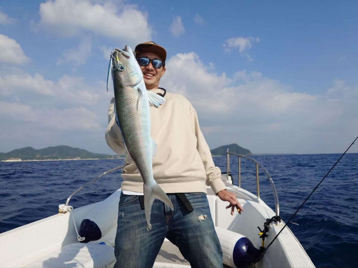 Angler holding an amberjack with green island hills behind