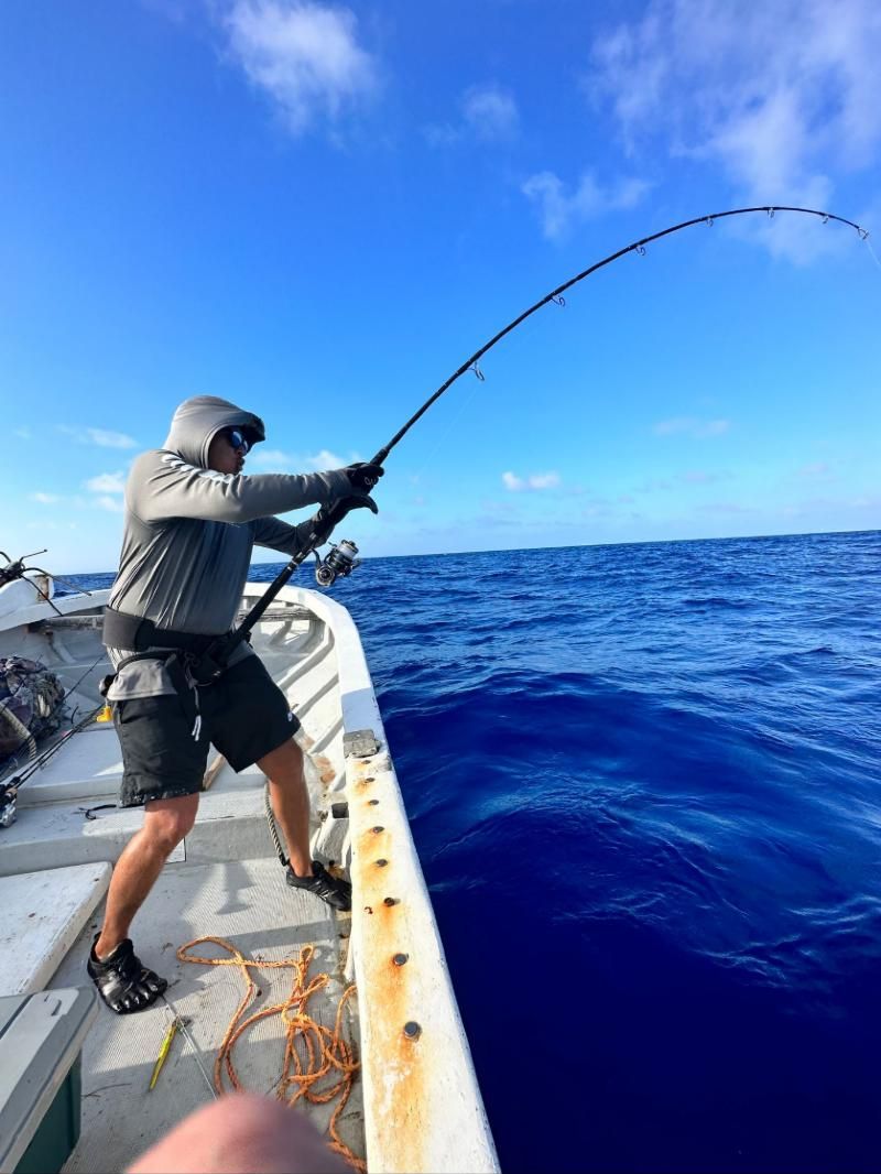 Angler in a fighting belt leaning back against a hard-bent rod on a small boat