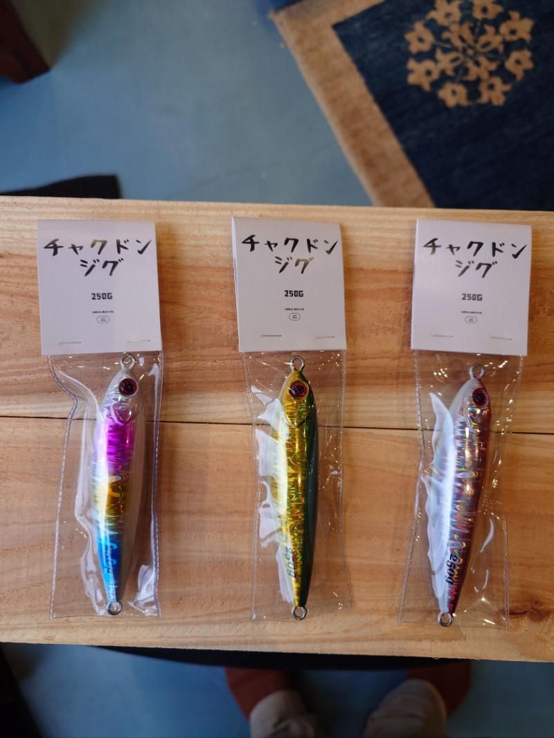 Three 250 gram metal jigs in pink, gold and silver on a wooden table