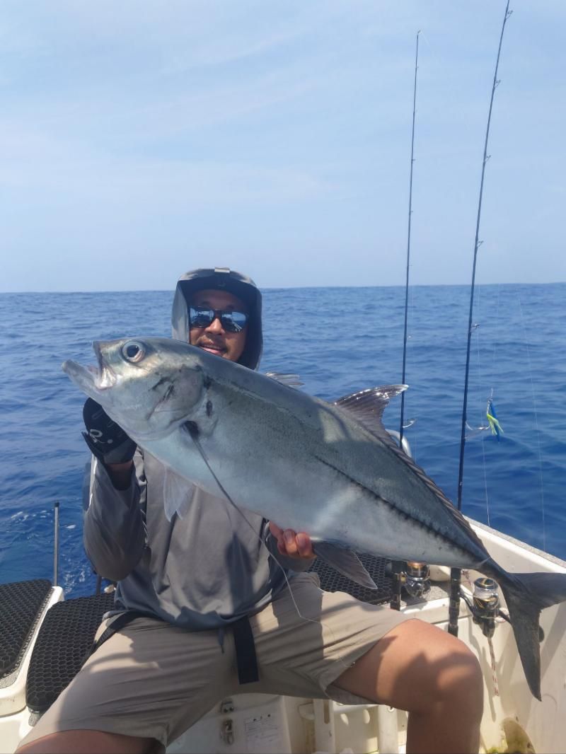 Angler holding a silver trevally on a boat
